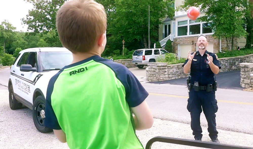 Young boy in a neon green shirt throws a red ball to a police officer on a quiet suburban street