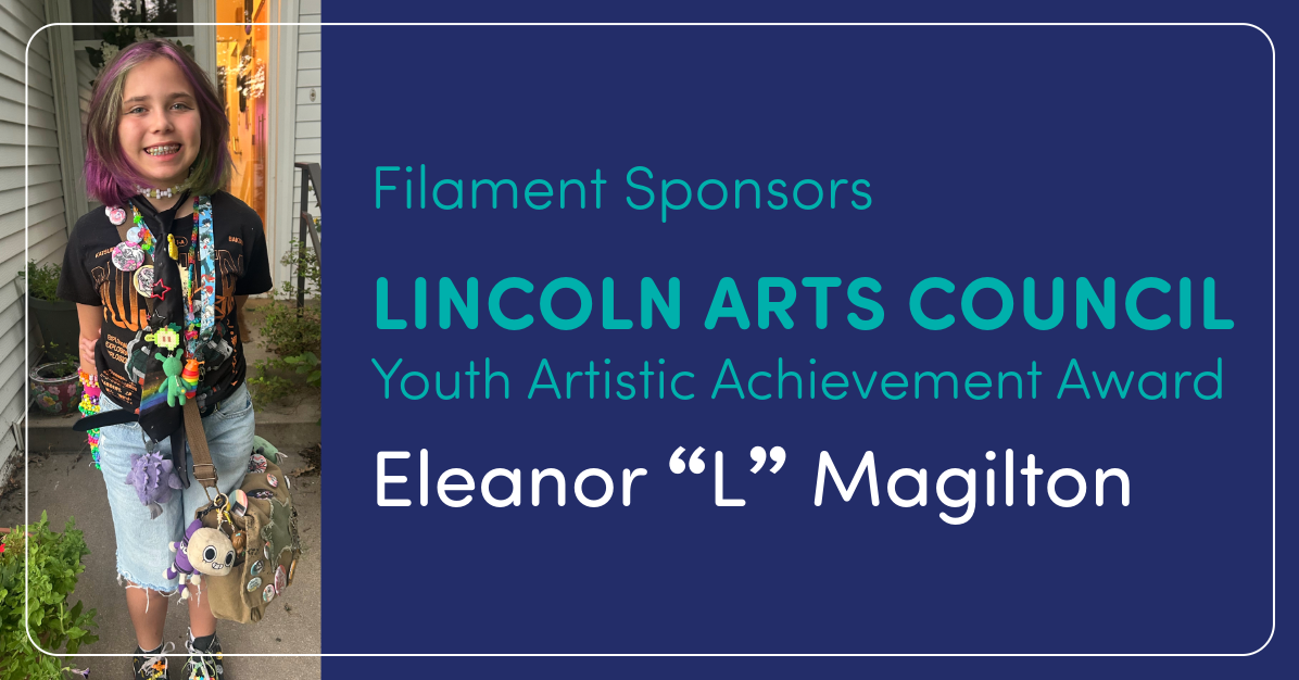 Young girl with colorful hair and lanyards stands beside a blue banner announcing the Lincoln Arts Council Youth Artistic Achievement Award for Eleanor L. Magilton.